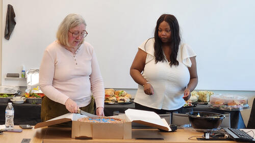 two people, one cutting a cake.