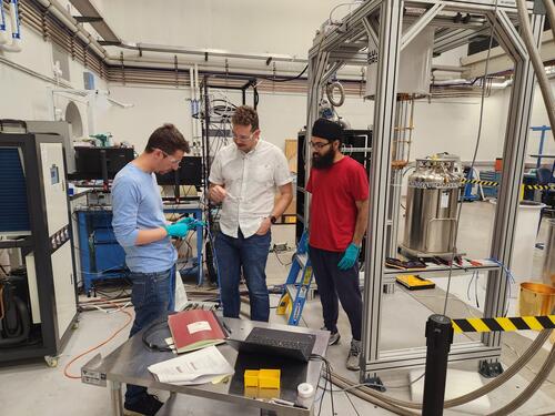 (L-R) Associate research scientist Mike Jewell, postdoctoral fellow Max Silva-Feaver, and graduate student Sukhman Singh work on wiring for ALPHA. Image of people in a research lab in  Wright Lab