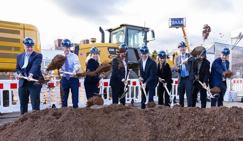 group of people with shovels in dirt wearing hardhats.